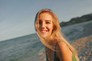 Outdoor summer image of sexy sportive blond woman posing on the beach. Wearing jeans shorts and green top. Fashion details. photo