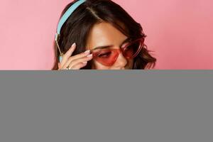 Studio fashion image of fascinating graceful woman in turquoise Panama and pink glasses listening to music by earphones. photo