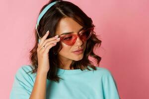 Studio fashion image of fascinating graceful woman in turquoise Panama and pink glasses listening to music by earphones. photo