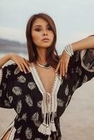 Close up portrait of  beautiful Asian woman in bohemian dress, ethnic jewelry and earring with feathers posing on the beach. photo