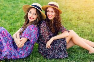 soleado verano retrato de dos alegre muchachas Gemelos sentado en verde prado y disfrutar hora juntos. foto