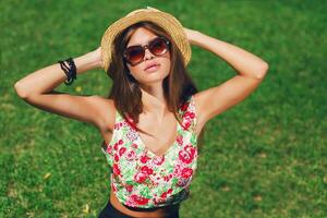 cerca arriba al aire libre retrato de seductor joven mujer sonriente , sentado en verde Fresco césped en soleado primavera parque . Perfecto bronceado piel. largo Delgado piernas. foto