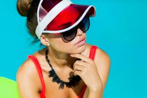 Sexy tanned    woman in red swimsuit having fun and enjoying  summer in amazing big swimming pool.  Stylish transparent cap. Beach party. photo