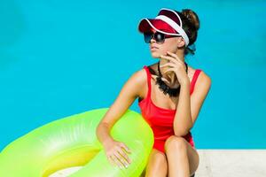 Sexy tanned    woman in red swimsuit having fun and enjoying  summer in amazing big swimming pool.  Stylish transparent cap. Beach party. photo