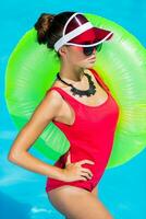 sexy bronceado mujer en rojo traje de baño teniendo divertido y disfrutando verano en increíble grande nadando piscina. elegante transparente gorra. playa fiesta. foto