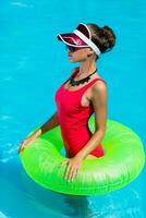 sexy bronceado mujer en rojo traje de baño teniendo divertido y disfrutando verano en increíble grande nadando piscina. elegante transparente gorra. playa fiesta. foto