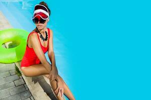 sexy bronceado mujer en rojo traje de baño teniendo divertido y disfrutando verano en increíble grande nadando piscina. elegante transparente gorra. playa fiesta. foto