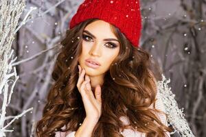 Close up portrait of  beauty  winter girl in frosty winter park .Beautiful young woman in red knitted hat, wavy  amazing hairstyle , full lips and  bright make up. photo