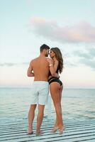 Outdoor  fashion portrait of pretty sexy couple in love  hugs on  amazing tropical  beach, wearing stylish swimwear. photo