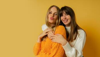 Close up portrait  of two pretty woman in cozy sweaters posing over yellow background.  Autumn and winter fashion trends. photo