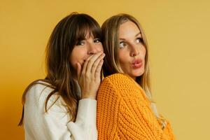 Close up portrait  of two pretty woman in cozy sweaters posing over yellow background.  Autumn and winter fashion trends. photo