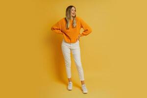 Blond  woman  with suprice face in orange  stylish autumn sweater posing over yellow background in studio.  Full lenght. photo