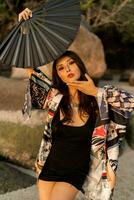 Close up portrait of seductive japanese girl in stylish  kimono  with large fan and professional make up posing on the beach. photo