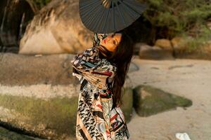 Close up portrait of seductive japanese girl in stylish  kimono  with large fan and professional make up posing on the beach. photo