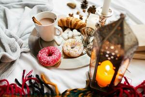 Still life with delicious Christmas gingerbread and cookies  breakfast on a tray in bed , donuts and croissants , cup of cacao or latte with cinnamon, ginger biscuits figure, Christmas candles. photo