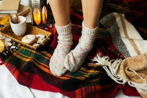 suave otoño retrato de bonito mujer sentado en su cama con libros y Bebiendo café con canela, galletas y vidriado donas detalles. foto