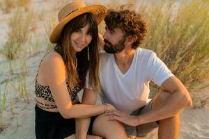 Traveling couple in love posing on the beach. Brunette woman in straw hat with her  boyfriend chilling in warm summer evening. photo