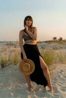 Cheerful brunette woman in stylish summer  boho outfit posing on the beach.  Sunset colors. photo