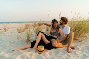 Stylish couple in love posing on the beach. Brunette woman in straw hat with her  boyfriend chilling in warm summer evening. photo