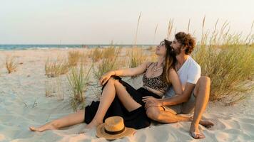 elegante Pareja en amor posando en el playa. morena mujer en Paja sombrero con su novio Relajado en calentar verano noche. foto