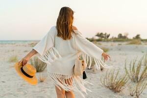 verano humor. juguetón morena mujer bailando en luz de sol en el playa. boho estilo. de moda collar y pendientes. ver desde atrás. foto