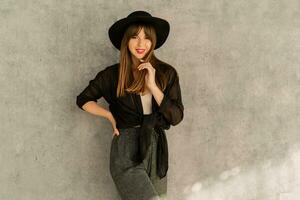 Fashion photo of stylish european woman with red lips in casual elegant autumn autfit. posing  over grey urban wall. Wearing black hat.