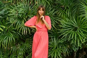 Romantic brunette woman in elegant pink dress  enjoing tropical vacations. Posing on green plants background. photo