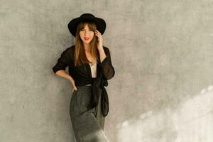 Moda foto de elegante europeo mujer con rojo labios en casual elegante otoño autfit. posando terminado gris urbano pared. vistiendo negro sombrero.