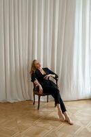 Indoor studio photo of elegant blond woman sitting on the chair. Casual  fashion look. Elegance, seductive mood.