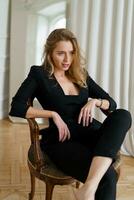 Close up studio photo of elegant blond woman with wavy blond hairs  sitting on the chair. Casual  fashion look. Elegance, seductive mood.