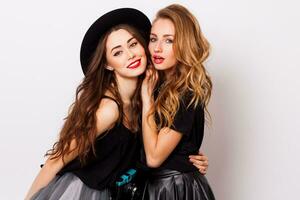 fashion portrait of two elegant stylish  women wearing a leather  skirt and black hat , holding  retro camera.  Posing against white background. photo