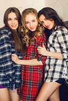 Close up indoor lifestyle portrait of three funny young friends have fun and pretending faces on the kitchen . Home party mood. Wearing plaid shirt. Warm soft photo. photo