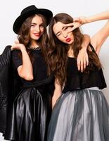fashion portrait of two elegant stylish women wearing a leather skirt and black hat. Posing against white background.They smiling and looking at camera. photo