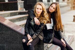 Two stylish  pretty  girls  posing on the street in sunny day. Wearing trendy urban outfit , leather jacket and boots heels. photo