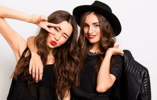 fashion portrait of two elegant stylish women wearing a leather skirt and black hat. Posing against white background.They smiling and looking at camera. photo