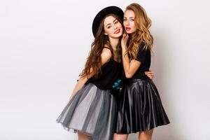 fashion portrait of two elegant stylish  women wearing a leather  skirt and black hat , holding  retro camera.  Posing against white background. photo