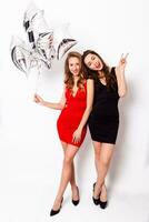 Two beautiful elegant women with red lips in evening black and red dress having fun. One keeping silver stars balloons in her hand . Two woman at the party. Inside. White background. photo