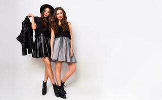 fashion portrait of two elegant stylish women wearing a leather skirt and black hat. Posing against white background.They smiling and looking at camera. photo