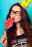 Studio closeup colorful portrait of young sexy funny fashion crazy  woman kiss big lollipop wearing summer  clothes ,  paper hat and cute glasses. photo