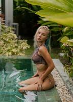 Gorgeous blond woman in sensual swimwear posing near pool on luxury tropical villa. photo