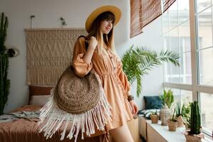 Woman sitting on bed in her boho apartments. Stylish decor, home plants. Cozy time. photo