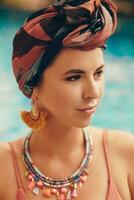 Woman with bright make up in bohemian outfit, turban, ethnic earrings, necklace and bracelets posing in swimming pool. photo