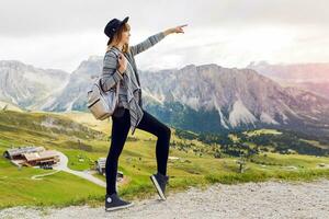 Young traveler woman with  hat and backpack enjoying amazing mountain view , walking and explore nature . Looking  forward . Shows a finger to the top. photo