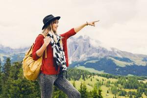 Outdoor spring  image of  traveler woman with hat and backpack enjoying amazing mountain view , walking and explore nature . Looking forward . Shows a finger to the top. photo