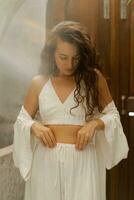 Romantic brunette female with perfect wavy hairs posing in  cozy boho interior. Wearing white linen costume. photo