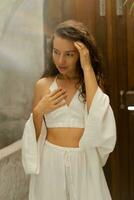 Romantic brunette female with perfect wavy hairs posing in  cozy boho interior. Wearing white linen costume. photo