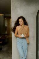 Stylish woman with perfect wavy hairs enjoying cup of coffee in modern cafe. Wearing trendy crop top and  jeans. photo