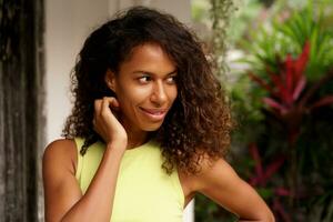 A close-up portrait captures the cheerful smile of a beautiful African American woman with dark skin, wavy hair, and  enchanting face as she poses in a tropical villa during  vacations. photo