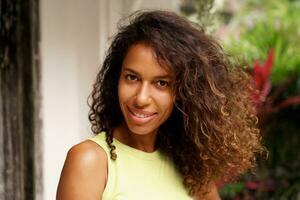 A close-up portrait captures the cheerful smile of a beautiful African American woman with dark skin, wavy hair, and  enchanting face as she poses in a tropical villa during  vacations. photo