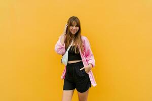 Charming brunette woman in stylish pink  linen  blouse  and black shorts posing on  yellow background. photo